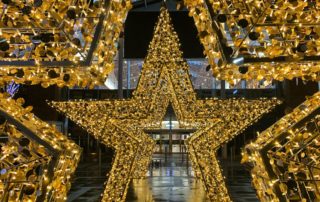 Three Light-up Gold Star Motifs displayed as a selfie point outside a shopping centre Christmas display.