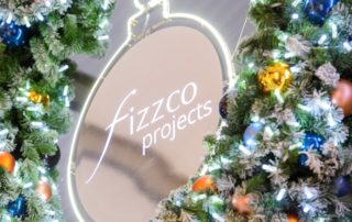 Light up artificial green wreath decorated with baubles and with Fizzco Projects logo in the centre.