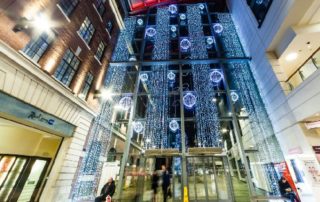 Bright white aurora balls and curtain lights displayed in the large window at the entrance to The Light Shopping Centre.