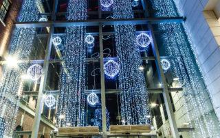 Bright white aurora balls and curtain lights displayed in the large window at the entrance to The Light Shopping Centre.