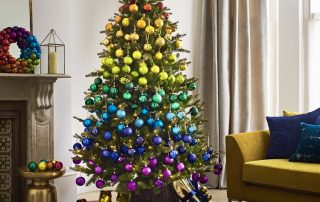 An artificial Christmas tree decorated with baubles in a rainbow colour scheme.