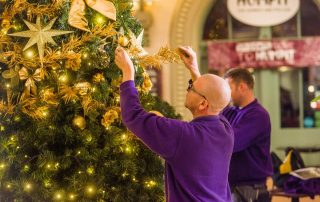 Fizzco installation team decorating a large artificial Christmas Tree with gold coloured Christmas baubles, bows, and foliage.