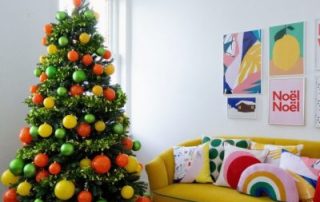 An artificial green Christmas tree decorated with yellow, orange and green baubles.