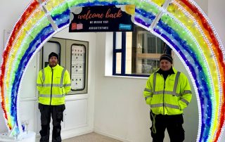 Light up rainbow arch displayed inside Alhambra Shopping Centre with two installers stood under the arch.