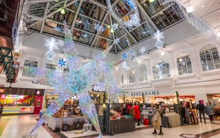 A shopping centre Christmas display featuring a large light up colour changing shooting star and bright white icicle lights around the wall of the centre of the Shopping Centre.