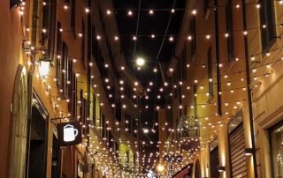 Warm white festoon lights draped above the footpath along a street.