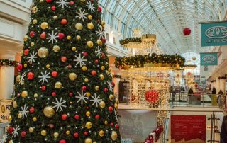 A traditional Christmas display at a shopping Centre featuring a large scale artificial cone Christmas Tree, Garlands and Chandeliers, with red and gold baubles and warm white lights.