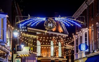 Christmas lights displayed outside in the Cornhill Quarter in lincoln, featuring bright white and warm white lights either side of the CQ sign, and warm white festoon lights zigzagged above the footpath.