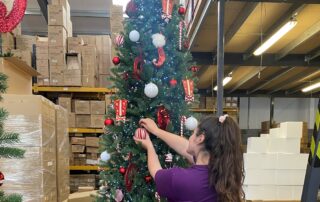 Warehouse team member decorating a Santa Suit themed Christmas Tree designed by Fizzco Projects.